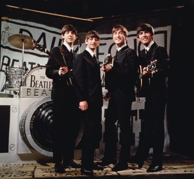 The Beatles performing on stage with a camera-shaped drum kit.