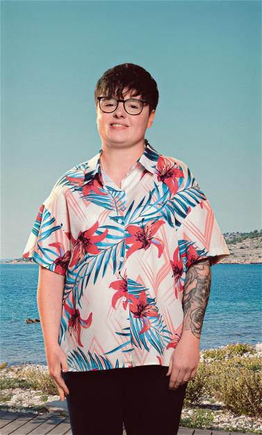 Person wearing a floral shirt and glasses in front of a blue sky and ocean.
