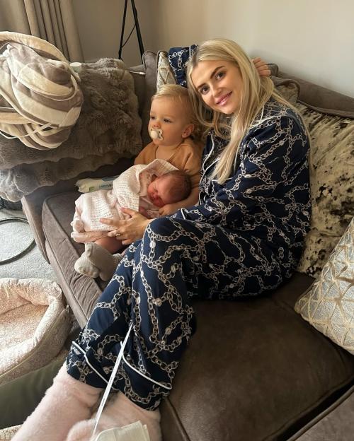 Lucy Fallon in pajamas holding a newborn and sitting next to a toddler.