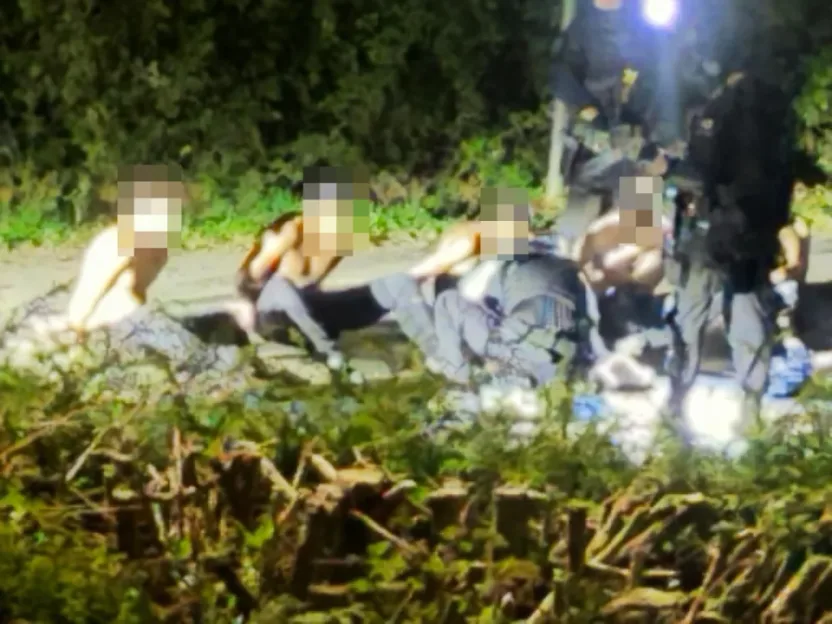Men with blurred faces on the ground, some shirtless, surrounded by others.