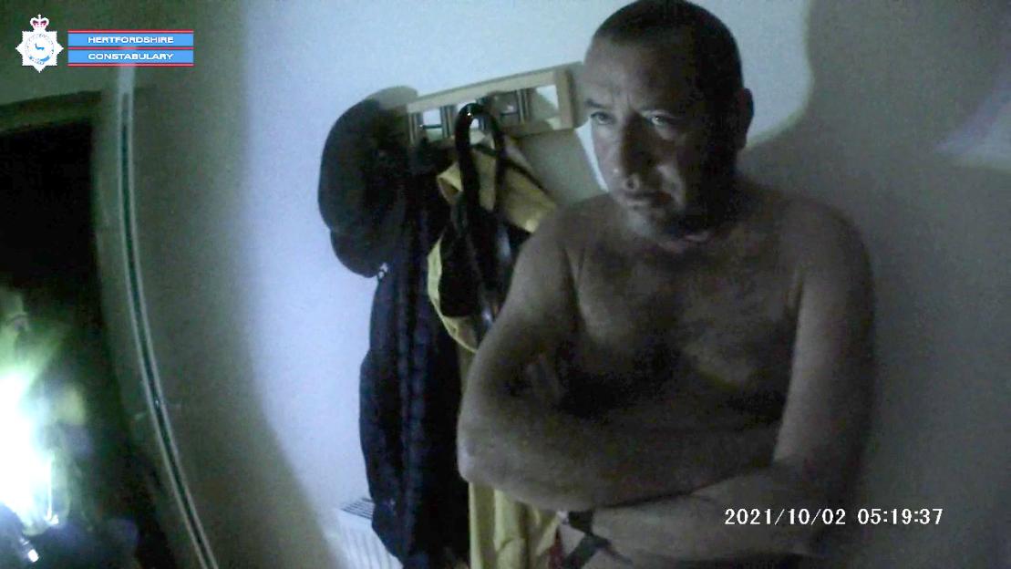 Police body camera footage of David Carrick, shirtless with his arms crossed, being arrested.