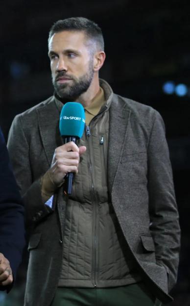 Three commentators holding microphones reporting on a football match.
