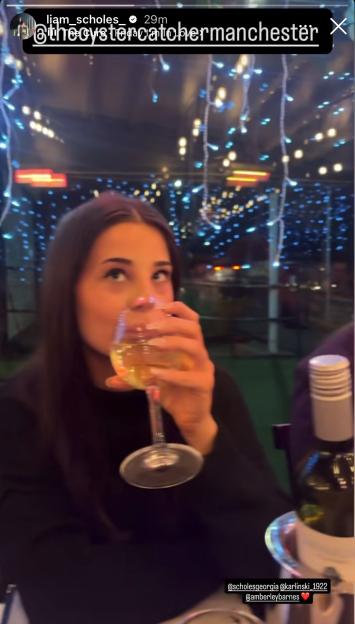 A woman, tagged as @scholesgeorgia, sips white wine, with blue string lights blurred in the background.