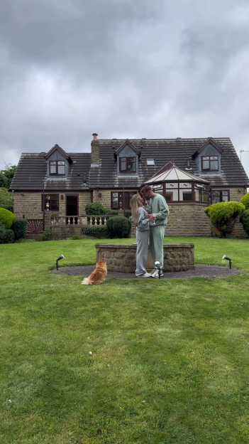 Molly Smith and Tom Clare kissing in front of their new house, with a dog sitting nearby.