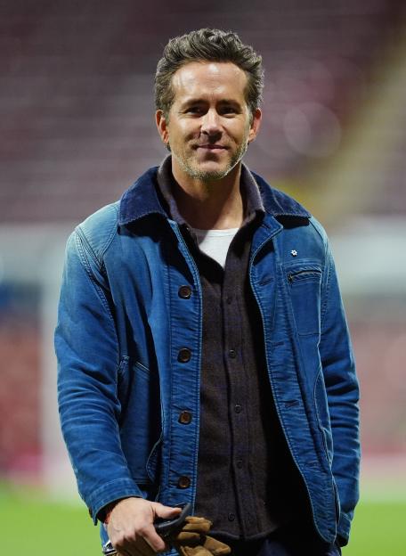 Ryan Reynolds in a blue denim jacket with a corduroy collar and a dark collared shirt.