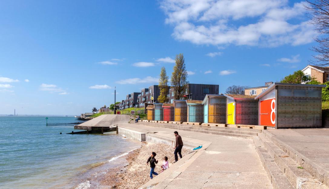 Long view of colorful beach huts, with housing in the background, by the water in Shoeburyness, UK.
