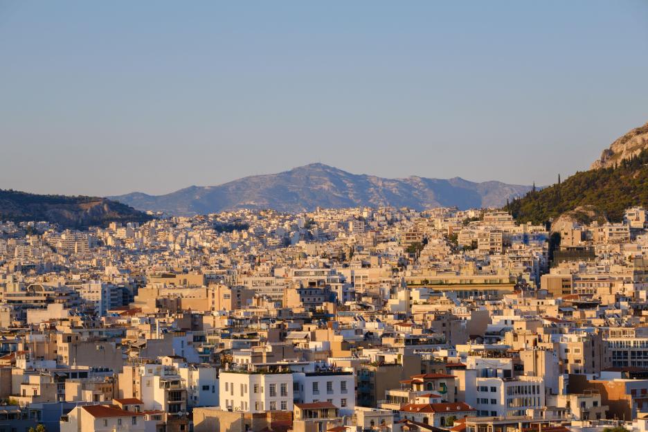 Panoramic view of Athens at sunset, with buildings sprawling across hills under a clear sky.