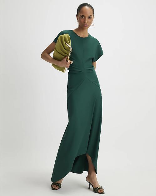 A woman models a green short sleeve cinched waist maxi dress with a chartreuse clutch and dark green heels.