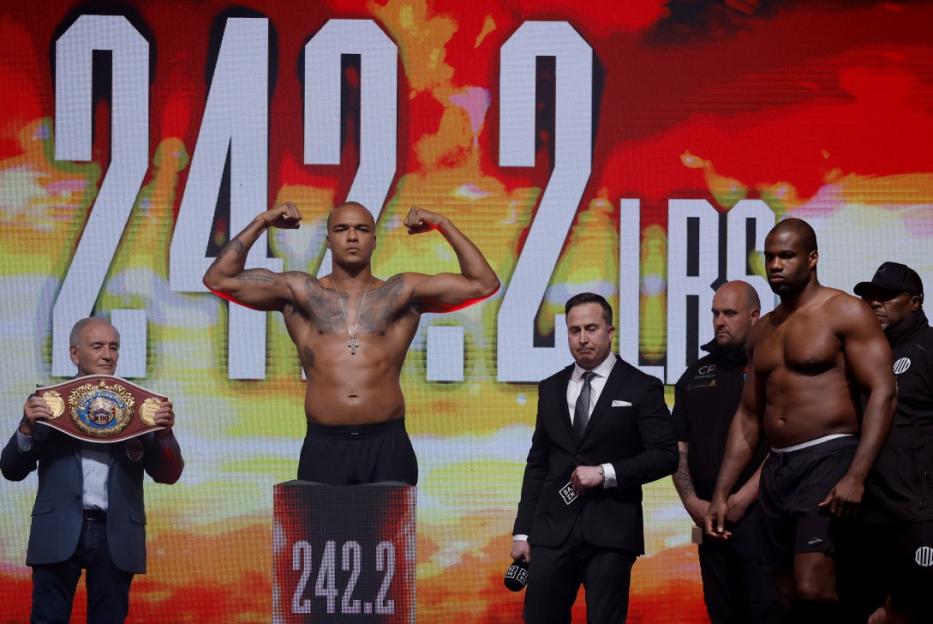 Fabio Wardley flexing on the scale, with Daniel Dubois standing nearby, during their weigh-in.