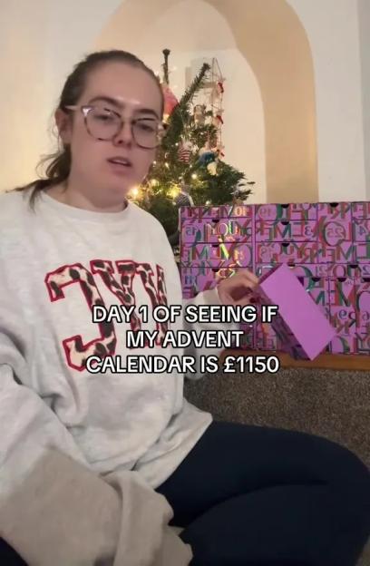 A woman opening an advent calendar, with a Christmas tree in the background.