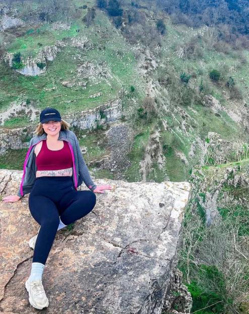 Charlotte Rutherford smiling while sitting on a rock overlooking a valley.