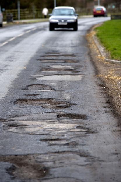 A car approaches potholes in Priory Road, Hull, East Yorkshire, UK.