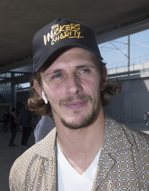 Jake Hall wearing a black cap with "The Wickers Charity" logo in gold.