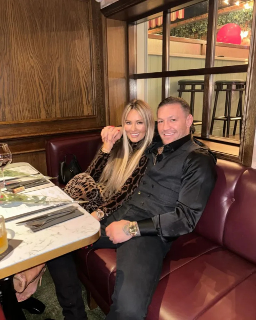 Conor McGregor and Dee Devlin sitting together on a red booth in a restaurant.