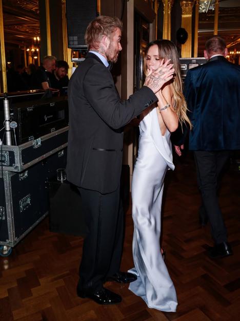 David Beckham holds Victoria Beckham's face while she smiles.