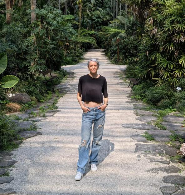 Woman standing on a path in a lush garden.