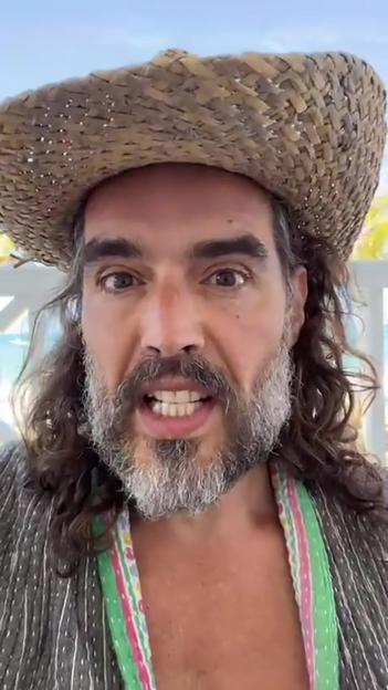 Russell Brand wearing a straw hat and green striped garment.