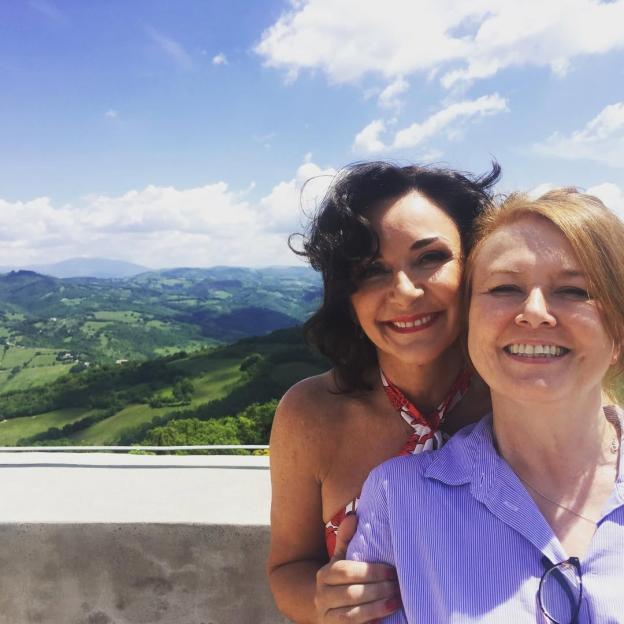 Shirley Ballas smiling while wearing a white dress with feather-trimmed sleeves.