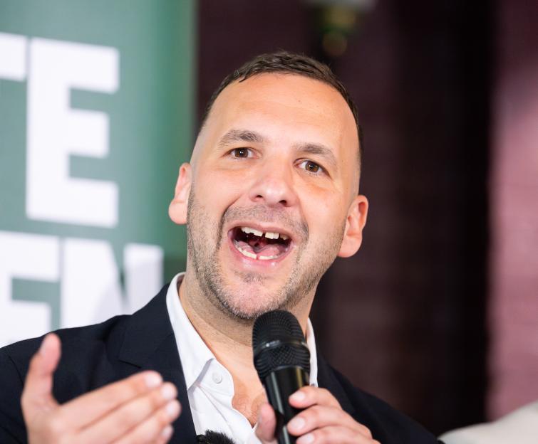 Green Party leader Zack Polanski speaking into a microphone at an event.