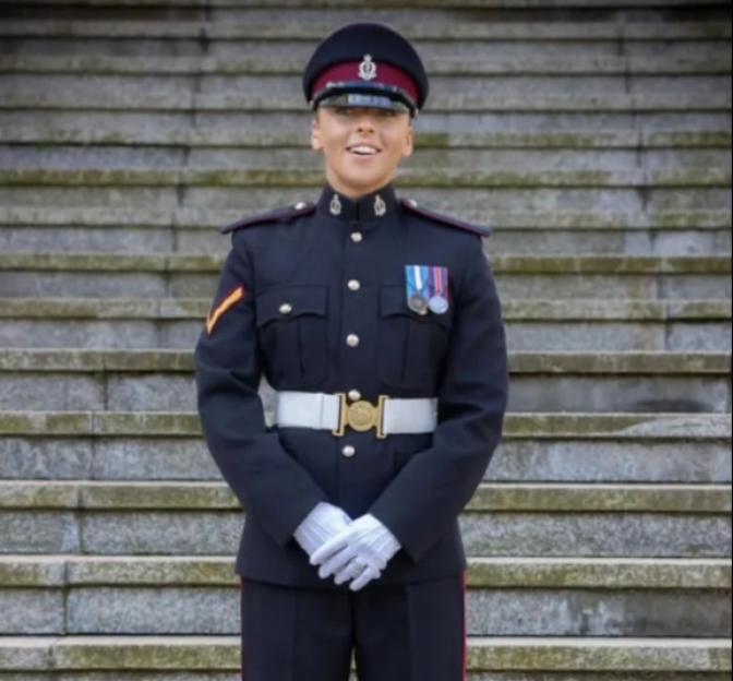 Lucy Wilde smiling in military fatigues from the open hatch of an old, weathered plane.