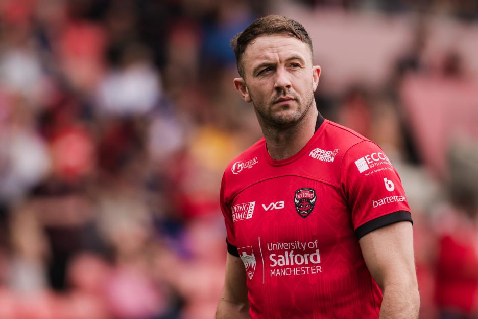 A rugby player in a red jersey with "Salford Red Devils" and "University of Salford Manchester" printed on it.
