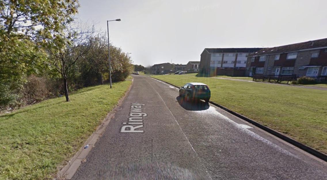 A paved road with "Ringway" painted on it, leading towards residential buildings.