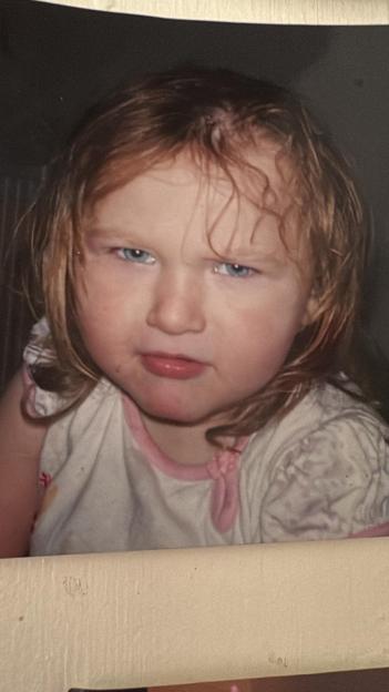 A young child with red hair and blue eyes, with a serious expression on her face.
