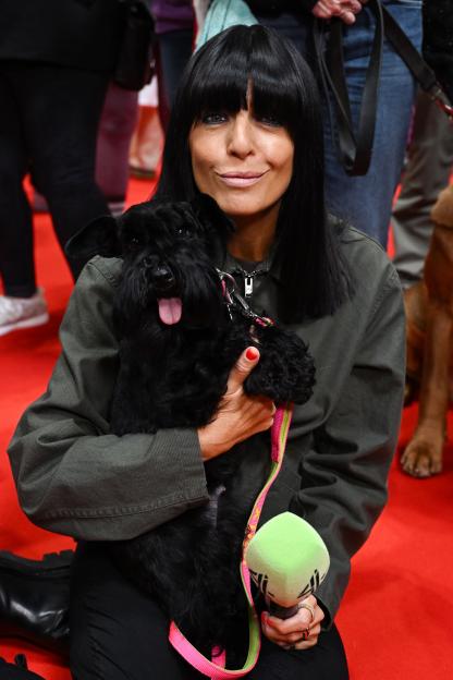 Claudia Winkleman holding a black dog and a microphone with a green foam cover.