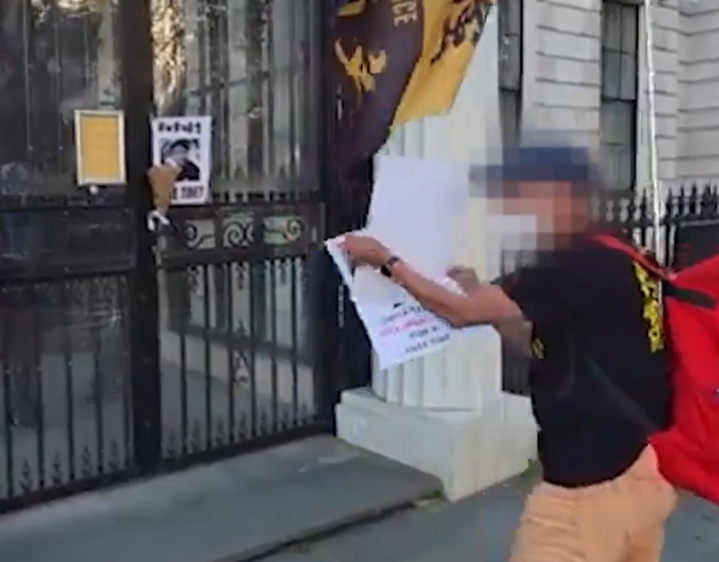 Person with a red backpack placing a poster on a black metal gate.