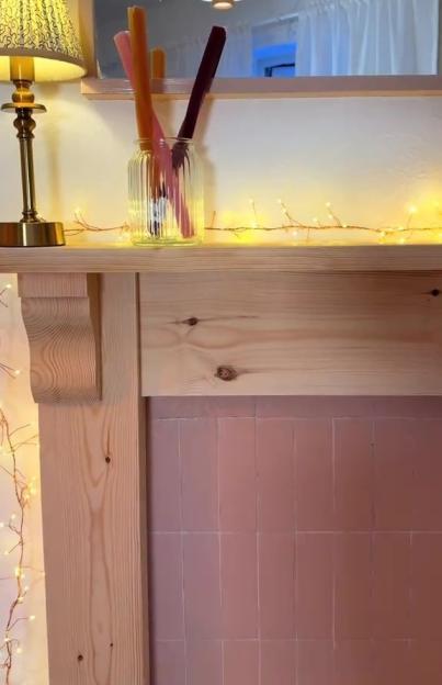 A faux fireplace with a wooden mantel, a tiled hearth, and string lights.