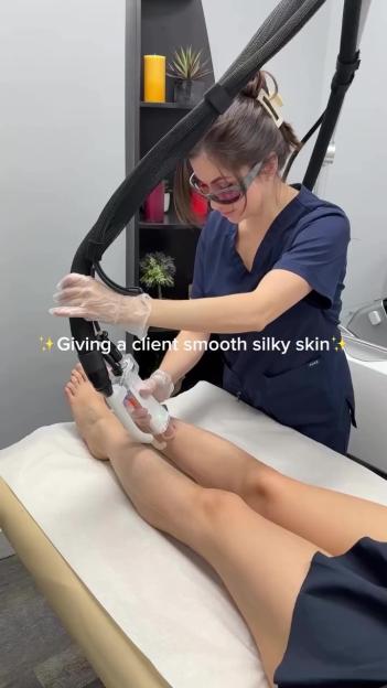 A woman in protective eyewear and gloves performs a laser hair removal procedure on a client's leg.