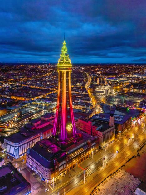 Aerial night view of Blackpool Tower illuminated in colorful lights, surrounded by the bright city lights of Blackpool along the Fylde Coast, Lancashire.