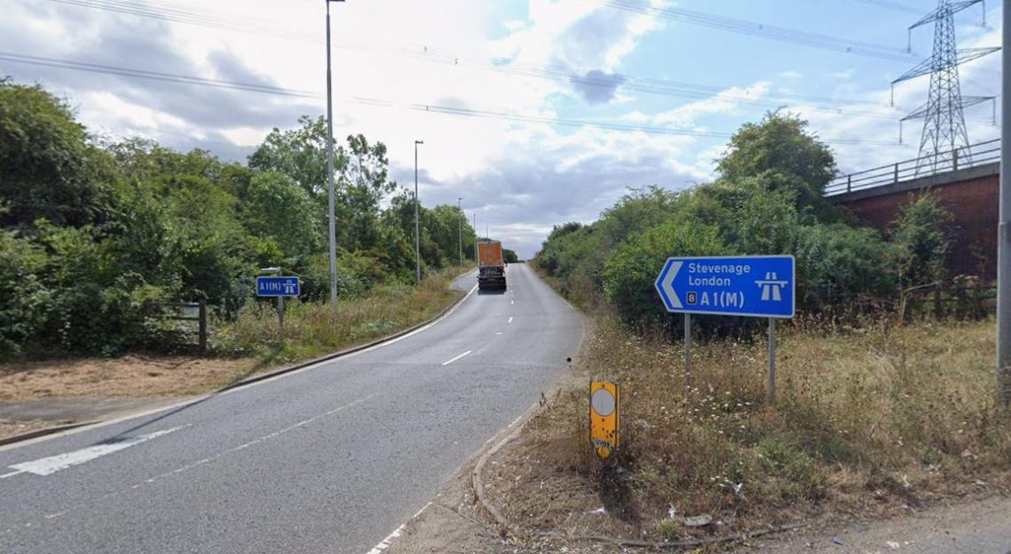 A blue road sign pointing left for Stevenage and London on A1(M), next to a highway.