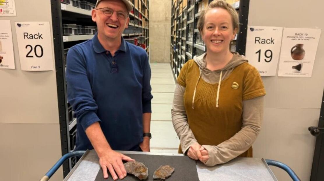 Two people smiling next to a display of rare 320-million-year-old fish fossils.