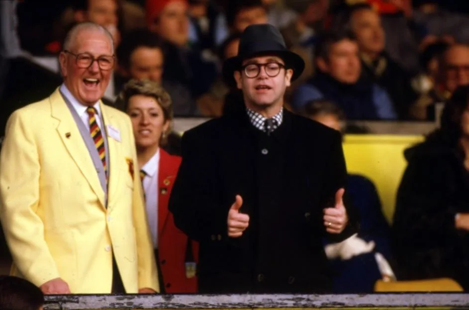 Elton John giving a thumbs up at a football match with Watford.