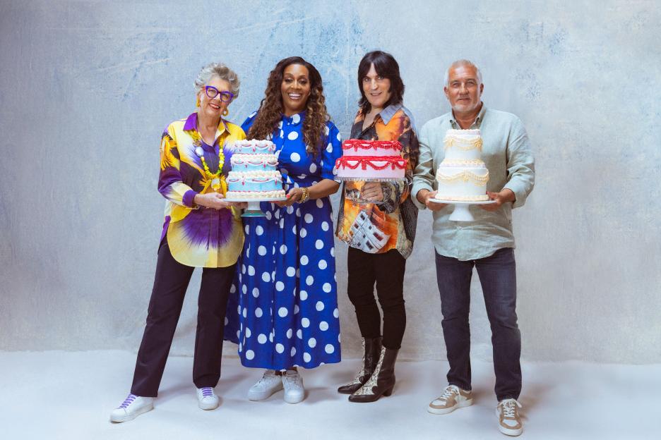 Alison Hammond, Noel Fielding, Prue Leith and Paul Hollywood from The Great British Bake Off holding decorative cakes.