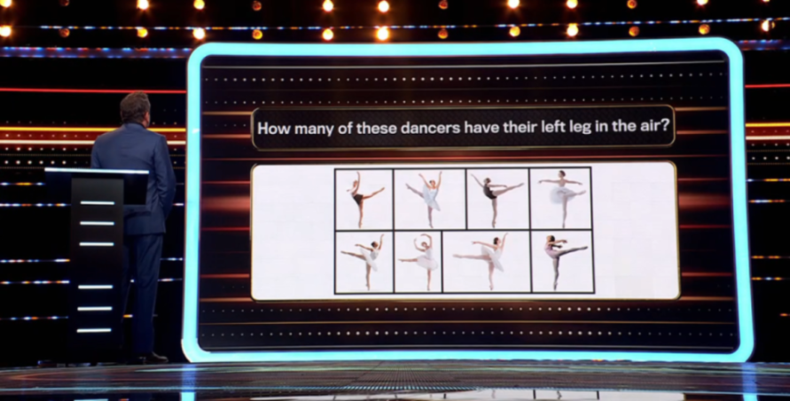 A man stands at a podium in front of a large screen displaying a trivia question: "How many of these dancers have their left leg in the air?" Below the question are six images of ballerinas in various poses.