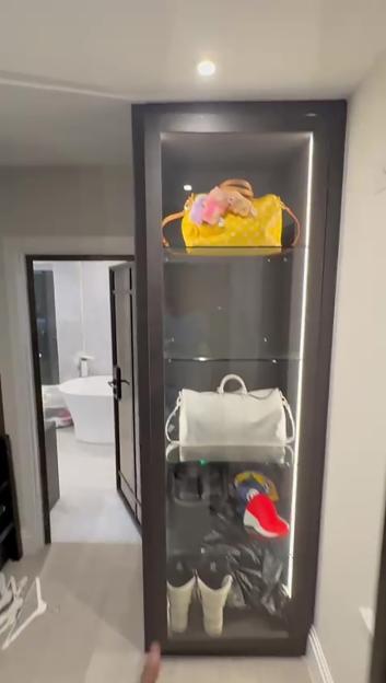 Glass display case of handbags and shoes with a bathroom visible in the background.