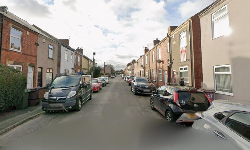 Residential street lined with parked cars and houses.