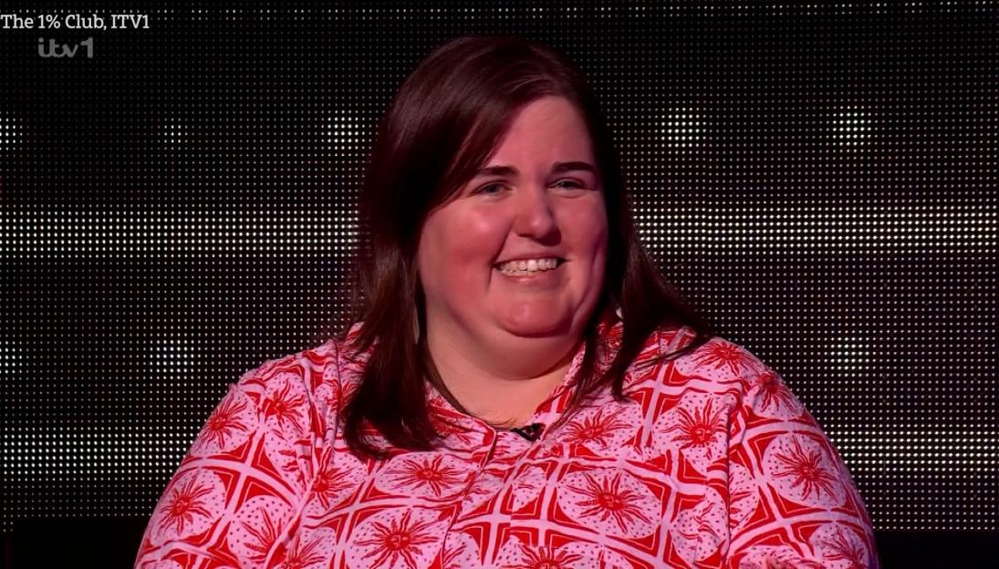 A smiling woman with long brown hair, wearing a red and pink patterned shirt, against a black background with white dots.