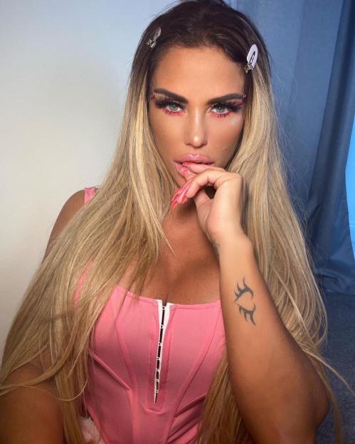 Katie Price in a pink corset, wearing pink makeup and hair clips, with a winged heart tattoo on her left arm.