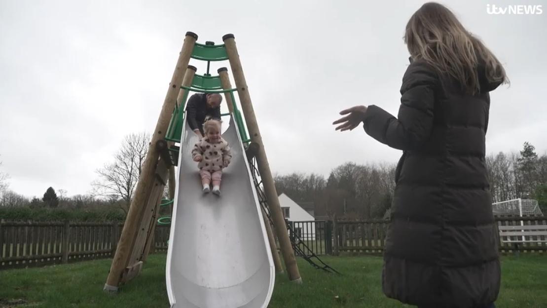 A smiling toddler, Leni, runs ahead of her parents, Gus and Emily, on a dirt path.