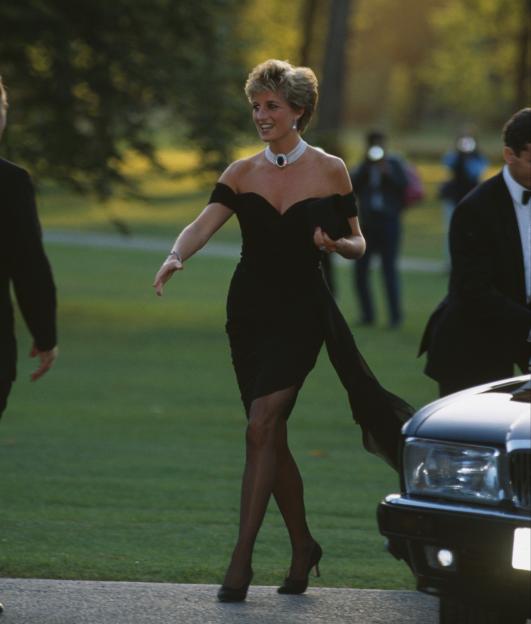 Princess Diana in a black Christina Stambolian dress, walking outside at a Vanity Fair party.