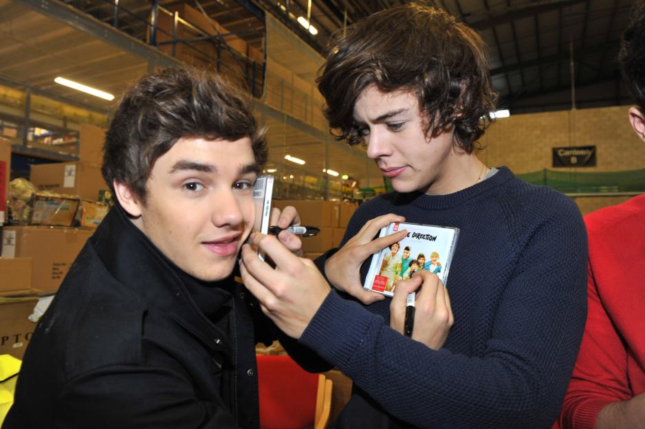 Liam Payne and Harry Styles signing copies of the One Direction album at an Amazon warehouse.