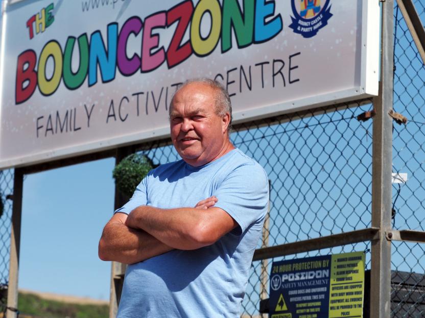 Lee Mahoney, owner of Bouncezone, stands in front of his business sign with his arms crossed.