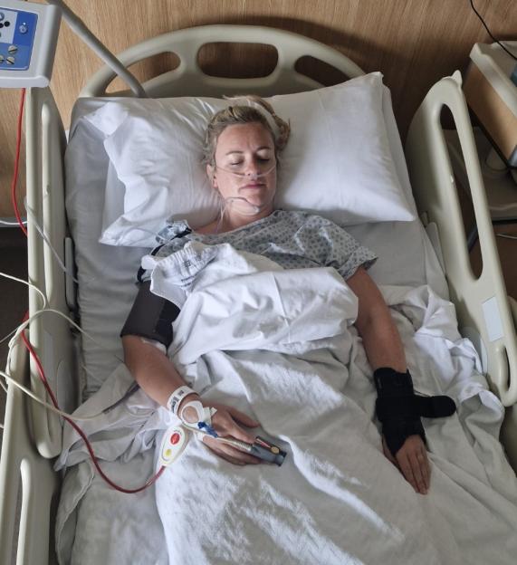 Woman lying in a hospital bed with a nasal cannula and a brace on her left wrist.
