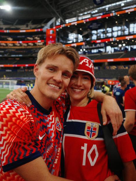 Helene Spilling and Martin Ødegaard smiling together in Norwegian football jerseys and a stadium in the background.