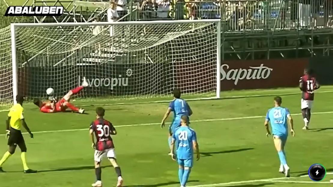 A soccer goalie in red saving a shot with his foot.