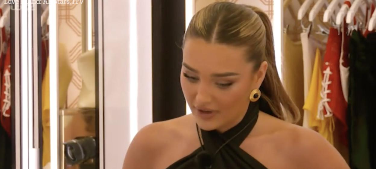 Belle Hassan with a ponytail, wearing a black halter top and large gold earrings, engaged in an argument on Love Island All Stars.
