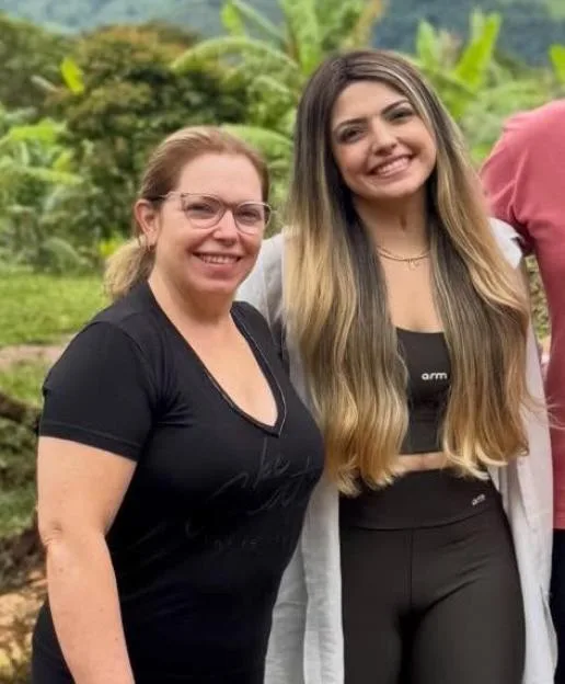 Two women smiling, one wearing glasses and a black shirt, the other with long blonde hair, a black crop top and leggings.